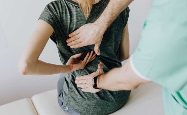 ragazza ha una postura scorretta quindi ha mal di schiena. Va dal medico a farsi controllare. Con la mano indica il punto della schiena che le fa male